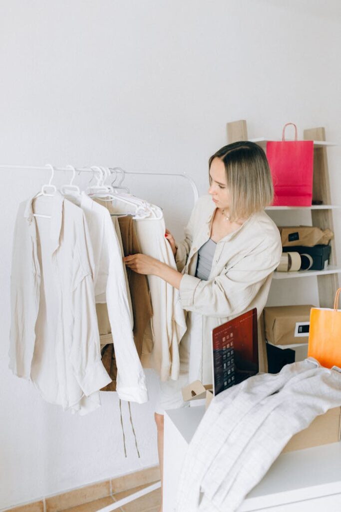 Woman browsing clothes online at home with shopping bags and laptop nearby.